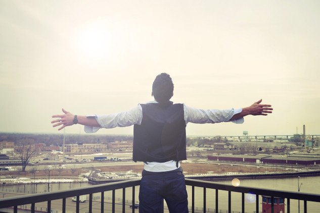 man standing looking out from a balcony with his arms wide open to the horizon