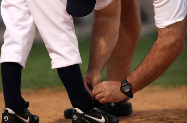 coach tying the shoe of a baseball player