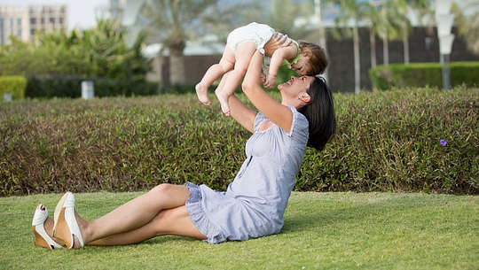 smiling mother, sitting on the grass, holding up a child