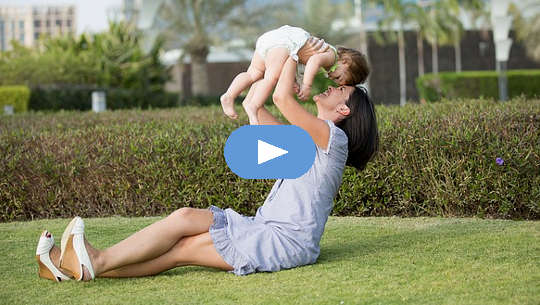 smiling mother, sitting on the grass, holding up a child