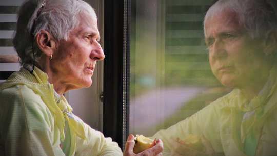 older person eating an apple and looking at her reflection in a window