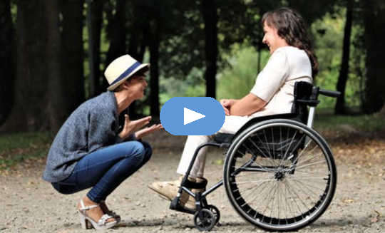 caring person squatting down in front of another in a wheelchair