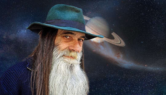 older long bearded man standing in front of a starry sky and planet