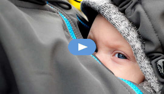 a baby sheltered inside his mother's jacket on her breast