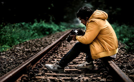 young man sitting on the railroad tracks looking at the pictures in his camera