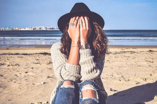 young woman sitting on a beach with her face hidden in her bands