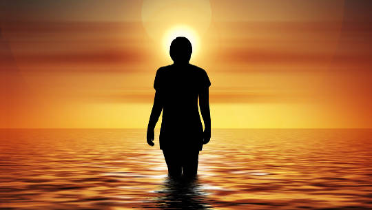 woman standing in the ocean looking at the rising sun