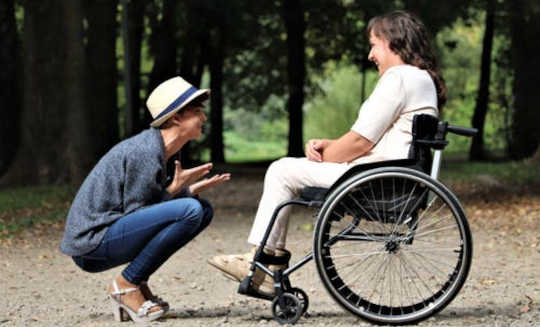 caring person squatting down in front of another in a wheelchair