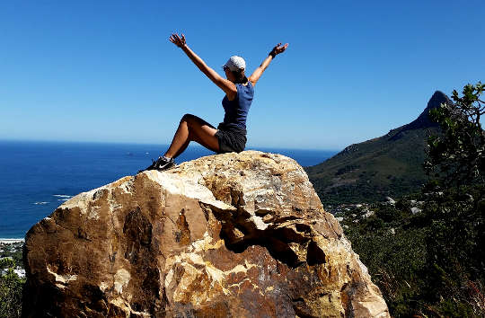 hiker sitting on top of a huge rock with arms up in the air in triumph