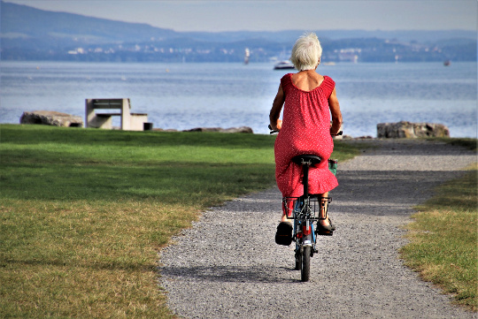 a senior woman with white hair and a red dress riding a bicycle