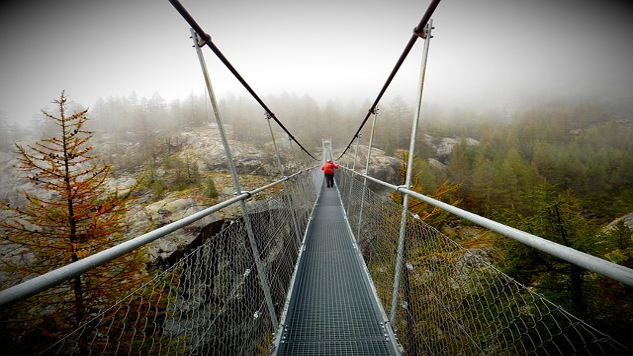 a rope bridge over a chasm with one person in the middle of the bridge