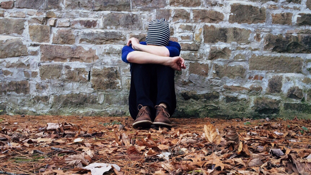 youth sitting alone outside with his head down on his arms