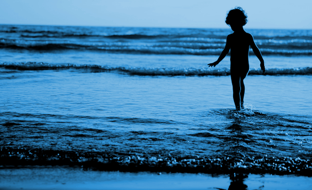 young boy standing in the water at the edge of the waves rippling in