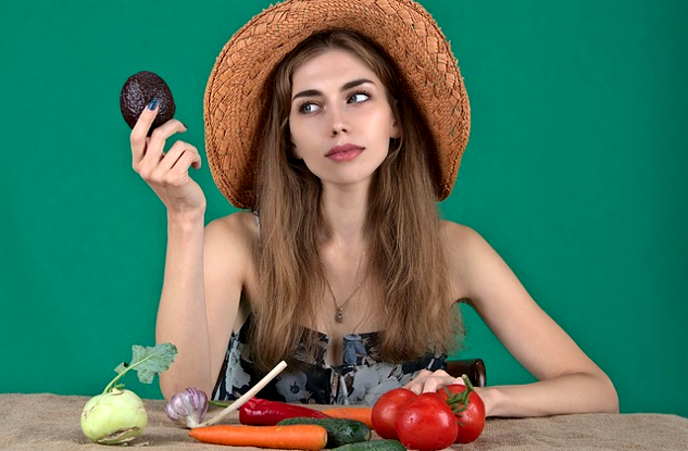 a woman with an array of fresh vegetables in front of her and holding up an avocado