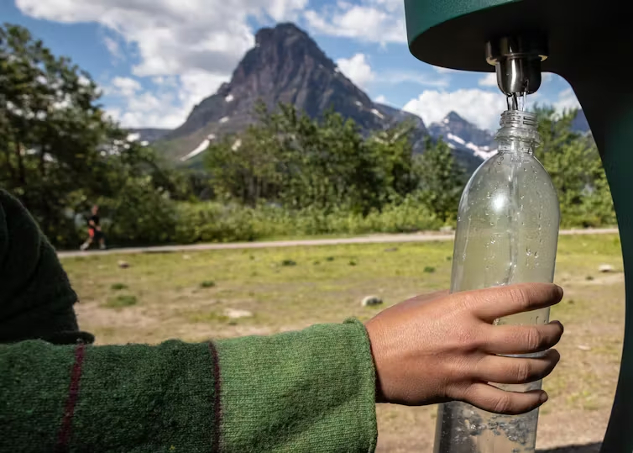 a person refilling a drinking water bottle from a outside spigot