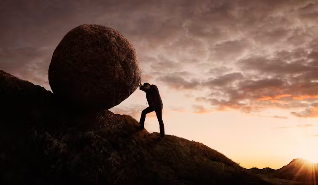 man pushing a boulder up a hill