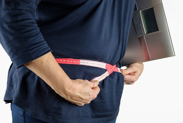 a person measuring themselves around the waist while holding a digital scale under their arm