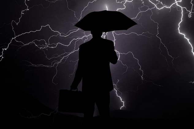 a businessman holding an umbrella over his head and facing a black sky filled with lightning