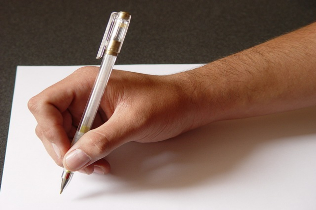 a picture of someone's hand holding a pen over a blank piece of paper