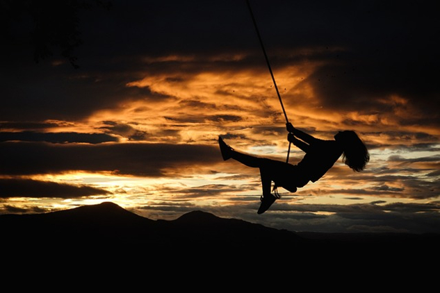 woman on a swing, happily swinging through the air. at sunset