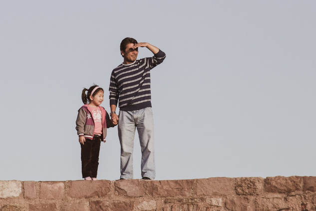 a father and daughter standing on a stone wall with the father looking into the distance