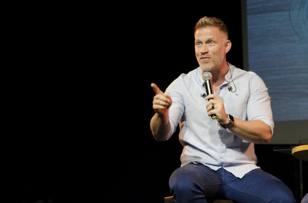 man holding a mic, on a stage speaking dynamically