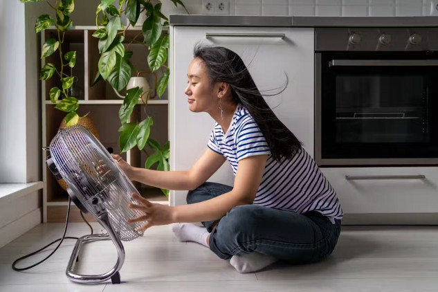 A young woman sitting close to a large electric fan. Not the most effective way to cool down