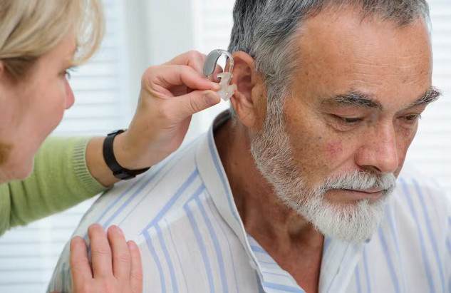 A doctor assists an older man with a hearing aid, a key tool in reducing dementia risk. Addressing modifiable risk factors like hearing loss can delay cognitive decline.