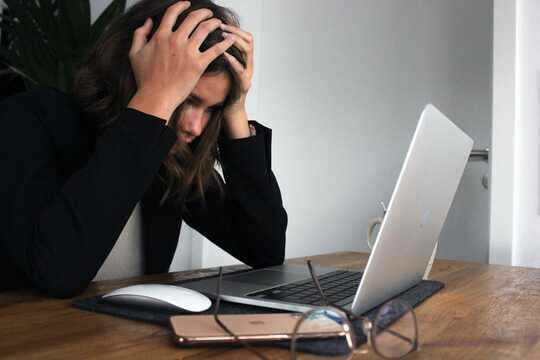 A woman with her head in her hands in front of a laptops